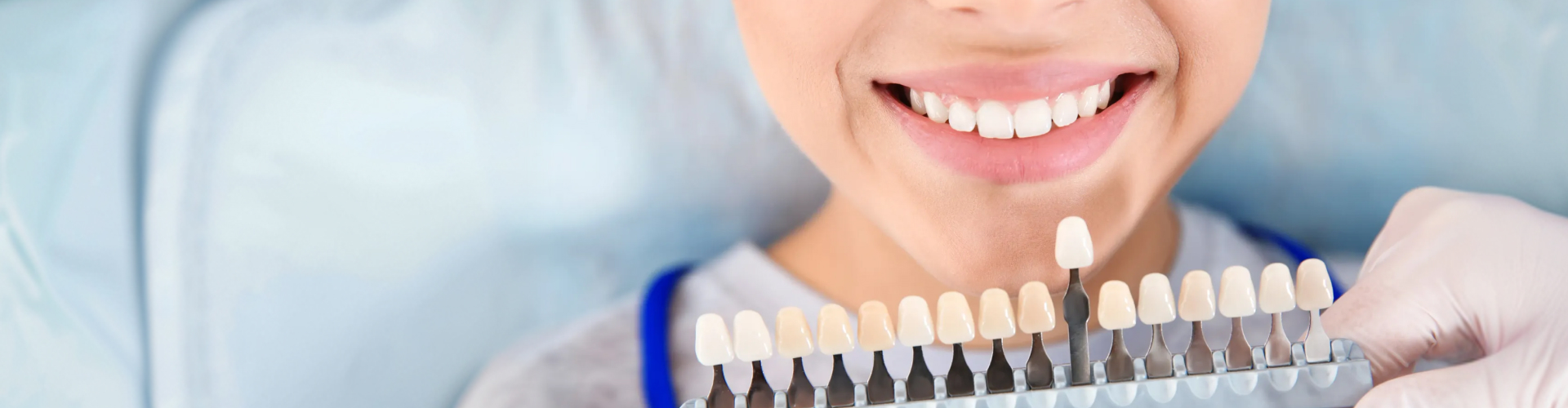 Gloved hands holding tooth shade-matching tool against woman's smile.